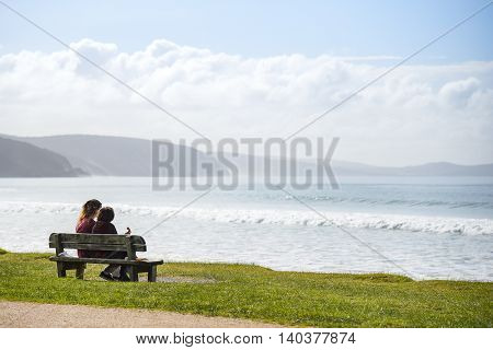couple people on wooden bench near beautiful beach landscape look out to sea in summer of Lorne (a town on Great Ocean Road route) Victoria Australia