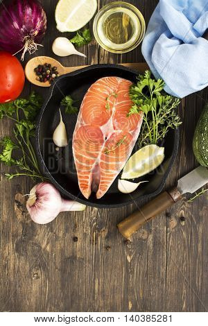 Raw salmon steak in an iron skillet with ingredients for healthy dinner. Top view