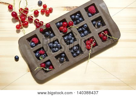 Diffrent types of berries in an ice cube tray with natural wooden background.
