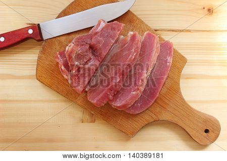 Fresh meat and a knife on a cutting board with wooden background.