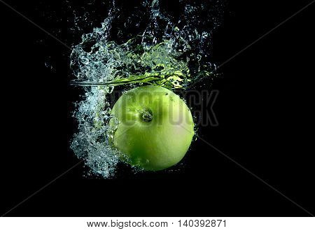 Green apple on black background with splashes