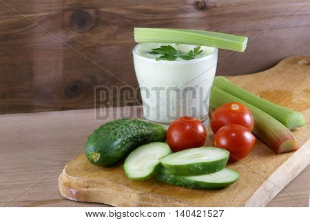 Useful summer snack: vegetables and yogurt sauce with herbs. Against the background of a rustic wooden table