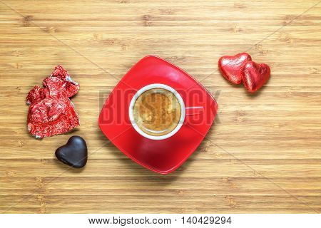 Heart shaped sweets wrapped in a bright red foil lying on a wooden texture with red cup of coffe near it. Background for romantic themes.