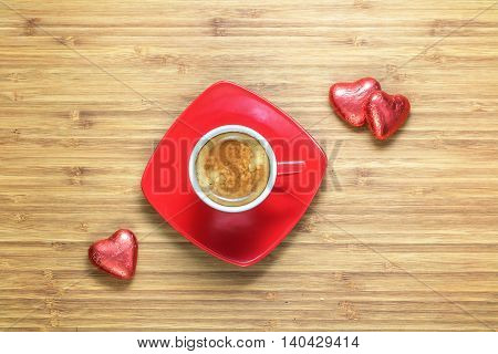 Heart shaped sweets wrapped in a bright red foil lying on a wooden texture with red cup of coffe near it. Background for romantic themes.