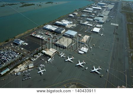 HONOLULU - APRIL 18: Aerial view of planes helicopters and cars parked by buildings by the runway at the Honolulu International Airport HNL next to the water on Oahu Hawaii. April 18 2016.