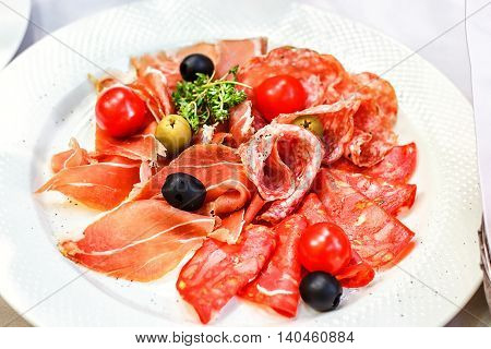 Italian salumi meat platter - prosciutto ham, salami olive and cherry tomato.