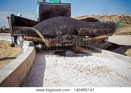 Front view on asphalt laying machine full of fresh asphalt at road construction site. Hot asphalt is spreading from paver machine on prepared ground.