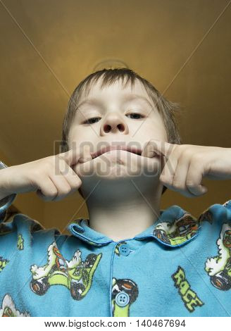 Boy make grimace on his face. Boy ape and make strange face. Boy try to scare with horror face