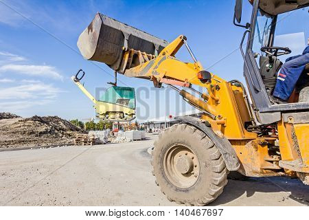Excavator is moving over building site with raised up front bucket vibration plate compactor machine is hanging.