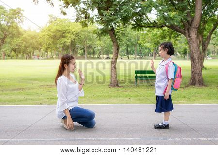 Back to school. Asian mother say goodbye to daughter student in park at school before study. Asian mother sent hand sign to goodbye.