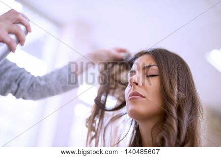 Hairdresser spraying his customer's hair.Young woman sitting while the hairdresser is styling her hair