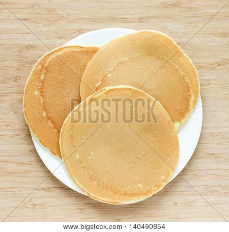 Golden pancakes on a white plate on a wooden background top view