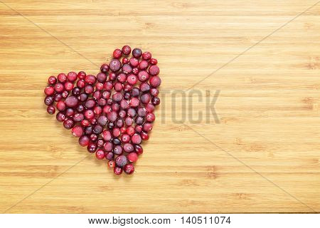 Cranberries in heart shape on wooden board with copy space, horizontal overhead view