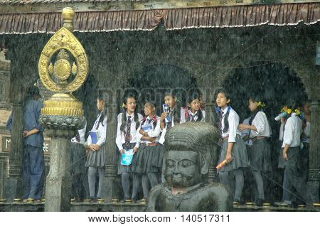 KATHMANDU CIRCA AUGUST 2012 - Young students shelter from the monsoon rain in a temple circa August 2012 in Kathmandu.