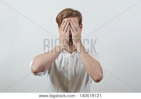 Young Adult Male Wearing White Shirt Covers His Face by Both Hands, Gesturing He Has Made a Big Mistake