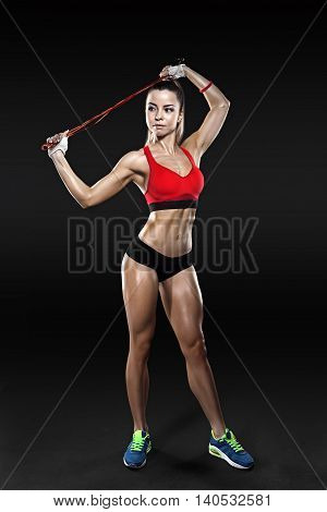 Shot of young female exercises with a jump rope looking at the camera. Muscular woman with skipping ropes against black background, with clipping pach, isolated.