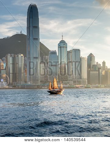 Old Junk on Hong Kong harbour with the sunlight hitting the sails and modern buildings in the background.