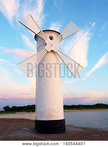 White old lighthouse decorated as windmill by sea on rocky coast. Seascape and landscape in background
