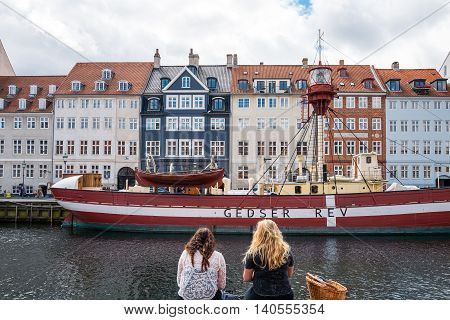 Copenhagen Denmark - July 20 2015: Two ladies sitting on the bank of the Nythavn canal with raditional houses and boats in the background