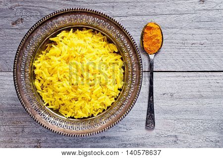 Top view of an antique metal bowl with cooked turmeric jasmine rice and vintage metal teaspoon with powdered curcumin