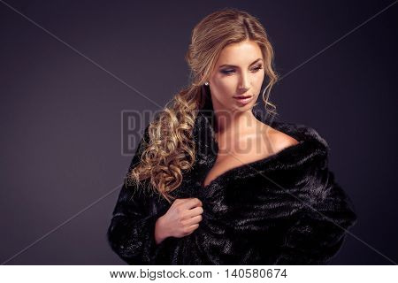 Fashionable young woman with long blonde hair smiling at camera while wearing black fur coat. Studio shot.Isolated.