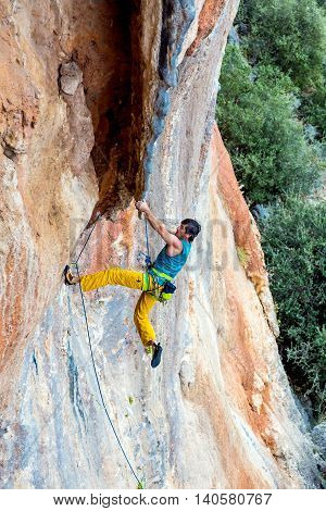 Man Climber Trying to keep Hold in last Effort to avoid deep fall down High rocky Wall orange and blue Colors Rope other Climbing Gear