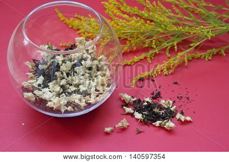 Jasmine Green Tea with dried flowers in a glass flask on a red background.