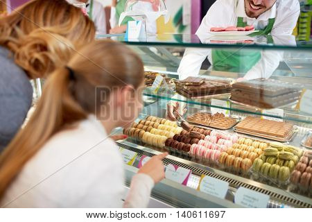 In pastry shop girl choose colorful macarons from showcase 