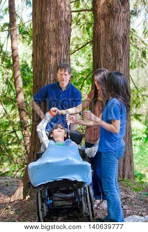 Family standing in woods giving tube feeding to disabled boy in wheelchair