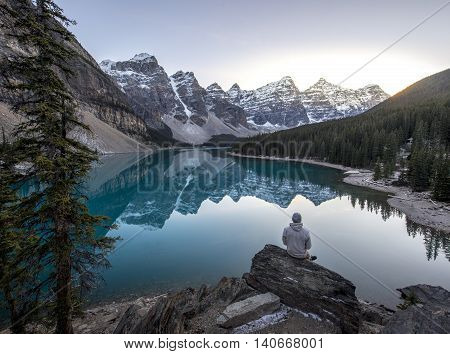 Young man sitting on a rock overlooking a beautful blue mountain lake