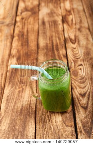 Jar tumbler mug with green smoothie drink over wooden background