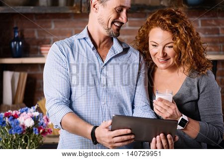 So interesting. Soigne surprised woman looking with interest at the tablet in hands of a satisfied man while being in the kitchen