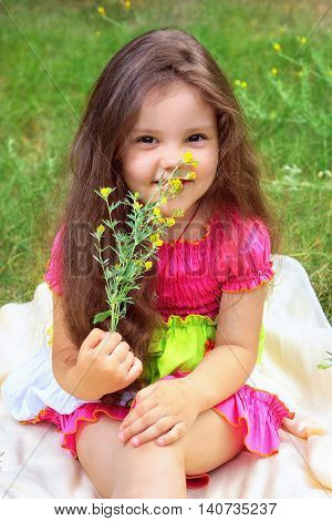 Pretty little girl smelling yellow flowers and sitting on a beige cover