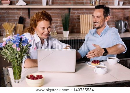 Look how cool it is. Smiling woman looking at the laptop while the man making a sign with a hand toward the screen