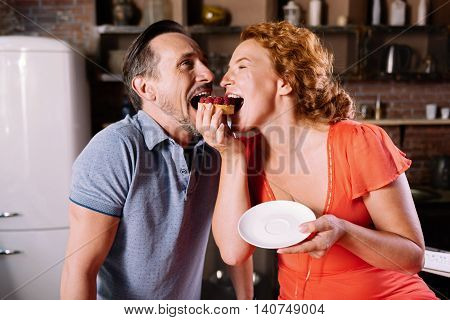Hey look. Joyful middle aged couple biting both the same cake with berries