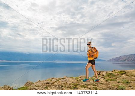 Woman hiker hiking with backpack looking at sea and mountains view. Recreation and healthy lifestyle outdoors in summer nature. Beautiful inspirational landscape. Trekking and activity concept.