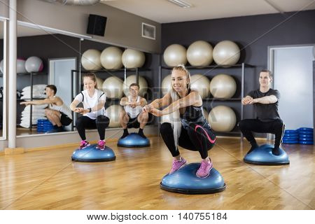 Woman Doing Squatting Exercise On Bosu Ball With Friends