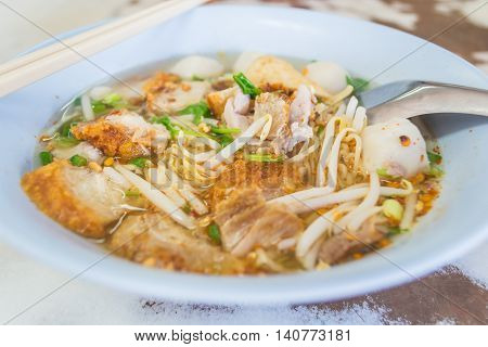 Spicy Thai Tomyum noodle with streaky pork vegetable and balls in a blue bowl.