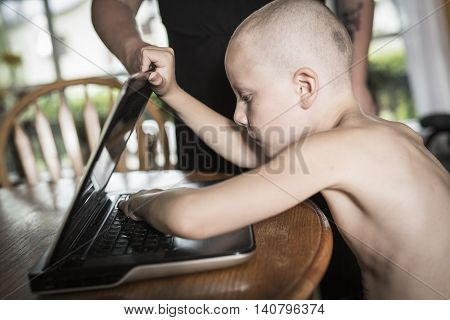 A boy with internet dependence playing with keyboard being dragged by mother from her computer