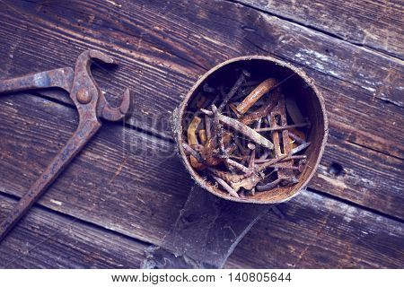 old rusty pinchers with can of nails on wooden boards background