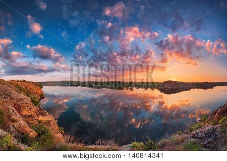 Beautiful panoramic landscape with colorful cloudy sky lake and mountains. Summer sunset at the river with clouds reflected in water. Panorama. Nature background