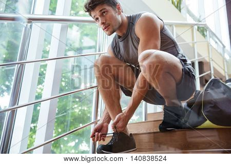 Handsome young man athlete sitting and tying laces on stairs