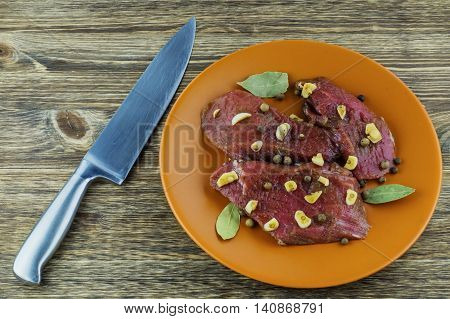 Marinated beef spices garlic and bay leaf on a ceramic plate. Raw veal meat steak and knife on a wooden table.