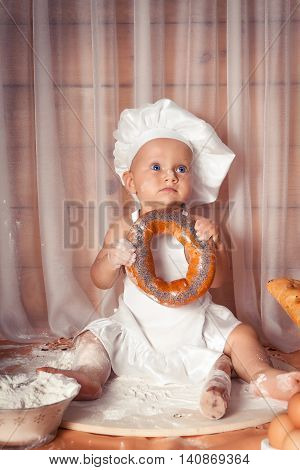 Happy baby baker sitting surrounded by bread and pastries