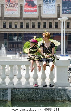 Kharkiv Ukraine - June 18 2016: Mother and daughter dreessed in costumes of bees are drying their feet after washing them in the fountain. Costumed bike ride 