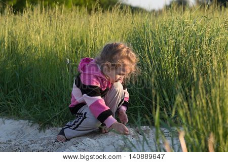 Hunkering little girl is playing in field dirt outdoors at natural green meadow grass backdrop