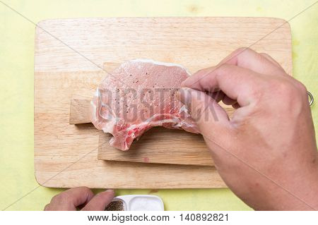 Chef putting pepper to raw porkchop / cooking porkchop steak concept