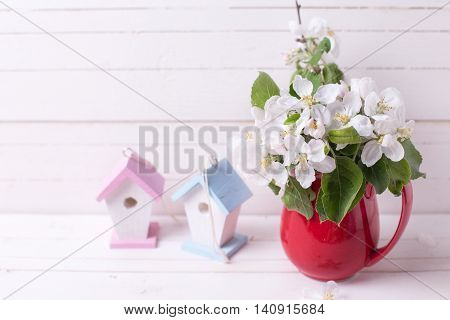 Tender apple tree flowers in white pitcher two decorative bird houses on white wooden background. Selective focus. Place for text.