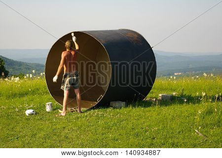 Man paints a rusty pipe in nature