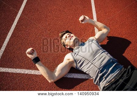 Fitness young man laying on running track after hard workout at the stadium